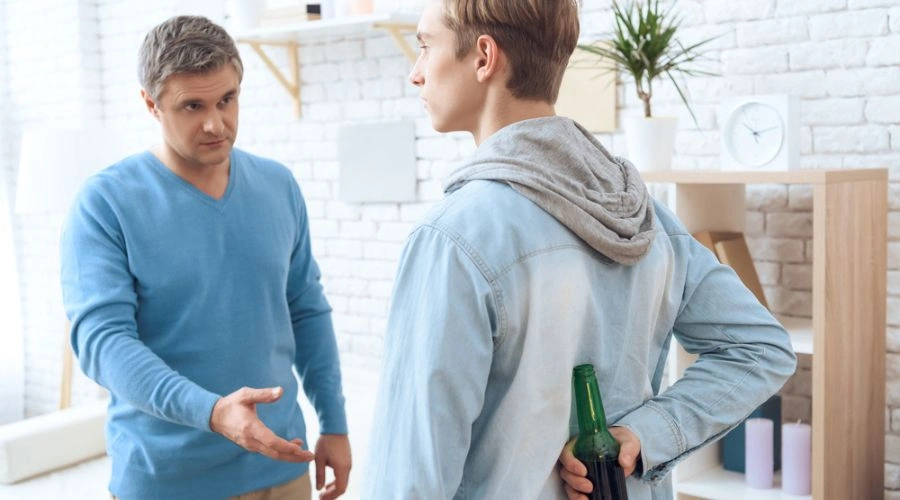 Parent speaking to son who has beer bottle hidden behind his back