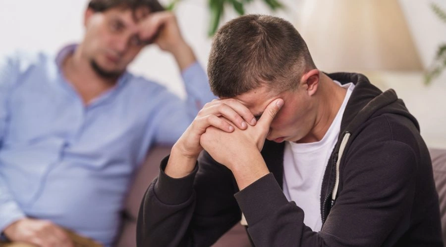Teen sitting with hands over his face as parent looks on - Early Detection Matters