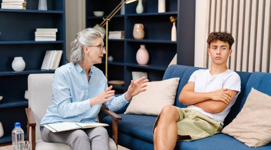 Image of Teen sitting on sofa talking to counselor in therapy -Early Interventions for Teens -Artemis Adolescent Healing Center