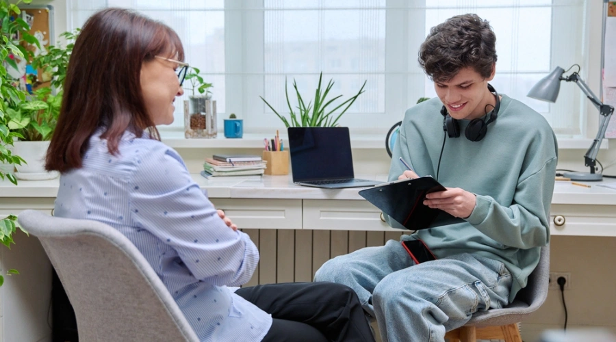 Image of male teen smiling, filling out a form as counselor looks on - Failure to Launch Therapy Program