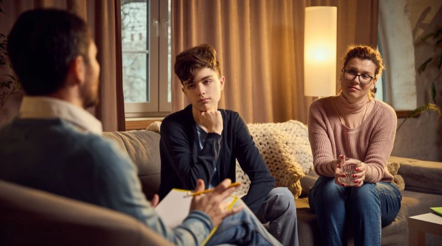 Image of teen in therapy talking to a counselor as his mother looks on