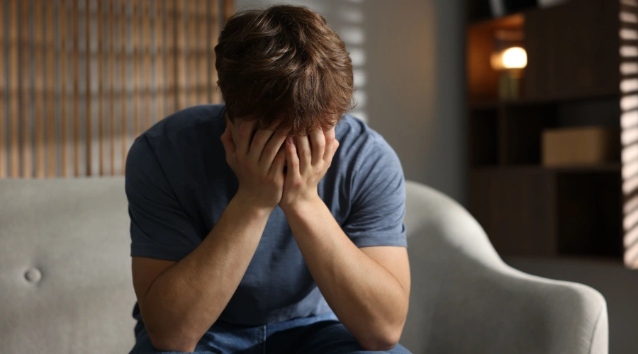 Image of a male teen sitting in a chair with both of his hands on his face - How Do Drugs Affect the Brain of A Teenager - Artemis Adolescent Healing Center