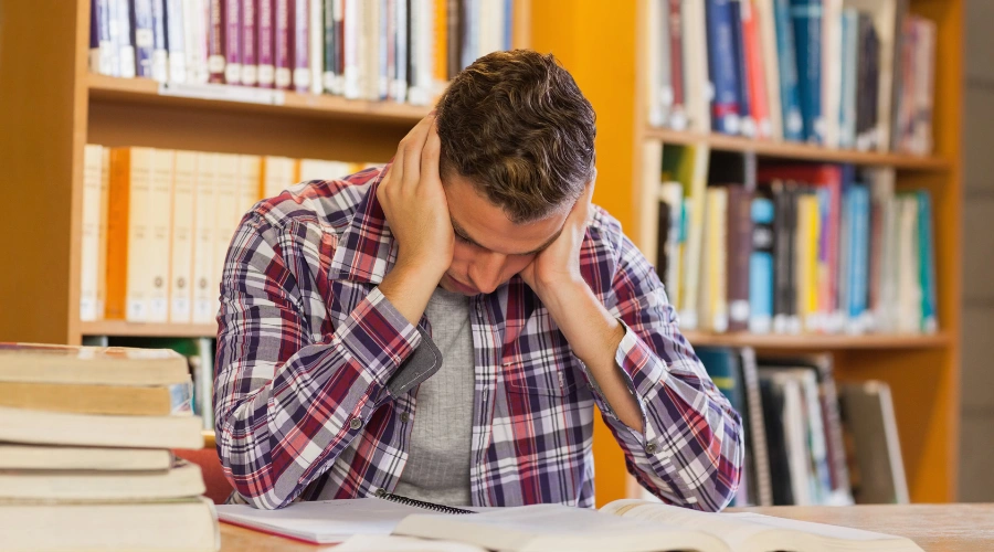Impact of a male teen sitting at a table reading with both hands on each side of his face - drug abuse on adolescent learning performance