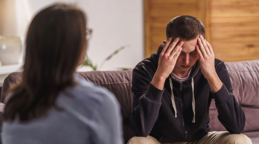 Image of distraught teen with hands on his face in therapy talking to a counselor - Meth Addiction Treatment for Teens