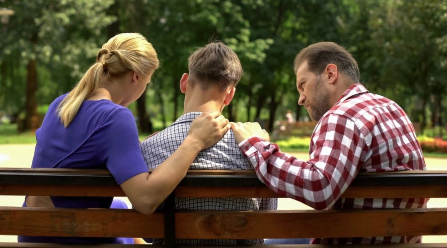 Image from behind of parents on each side of their son sitting on a bench - Role of Family in Teen Recovery