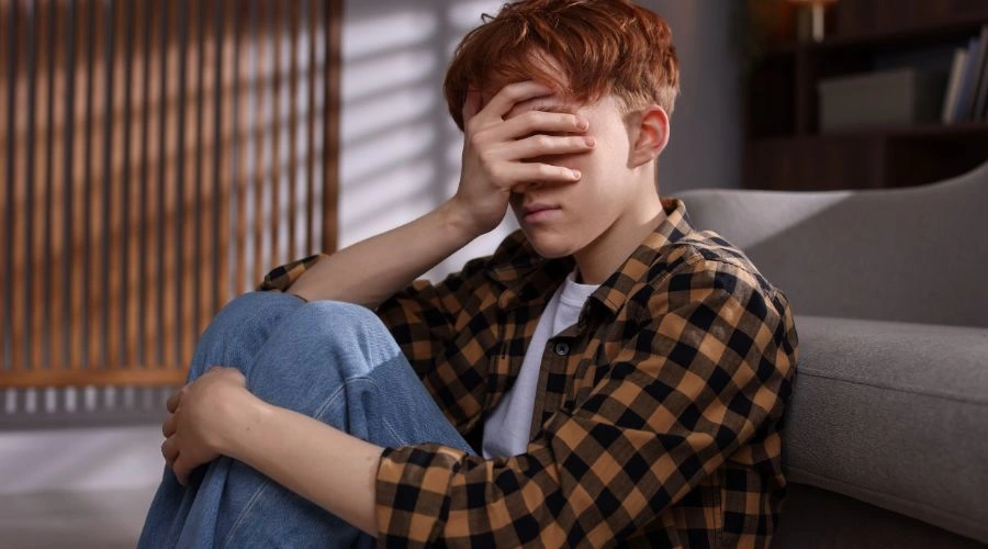 Image of a teen sitting on the floor with one hand covering his face - Signs and Symptoms of Schizophrenia
