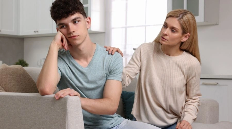 Image of a mother sitting consoling her unhappy teenage son beside her