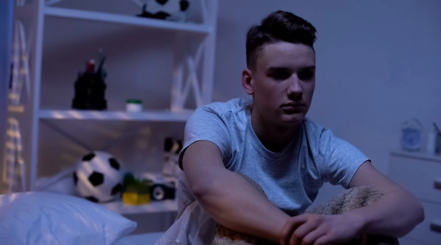 Image of bewildered teen sitting on his bed in dark room - Warning Signs that Teen Might Be Using Crystal Meth