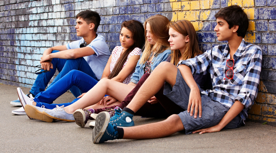 Image of two male and three female teenagers sitting beside a graffiti painted wall - What is considered an at-risk youth - Artemis Adolescent Healing Center