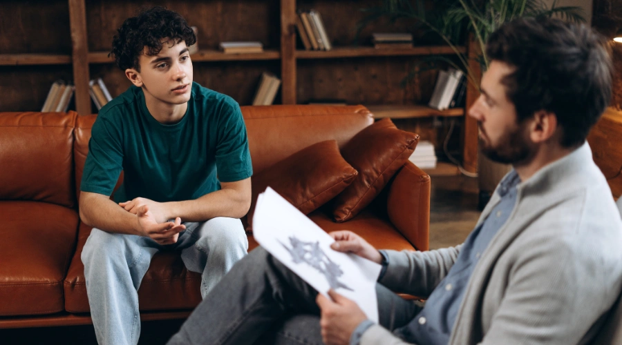 Image of a teen boy in a therapy session talking to his male counselor
