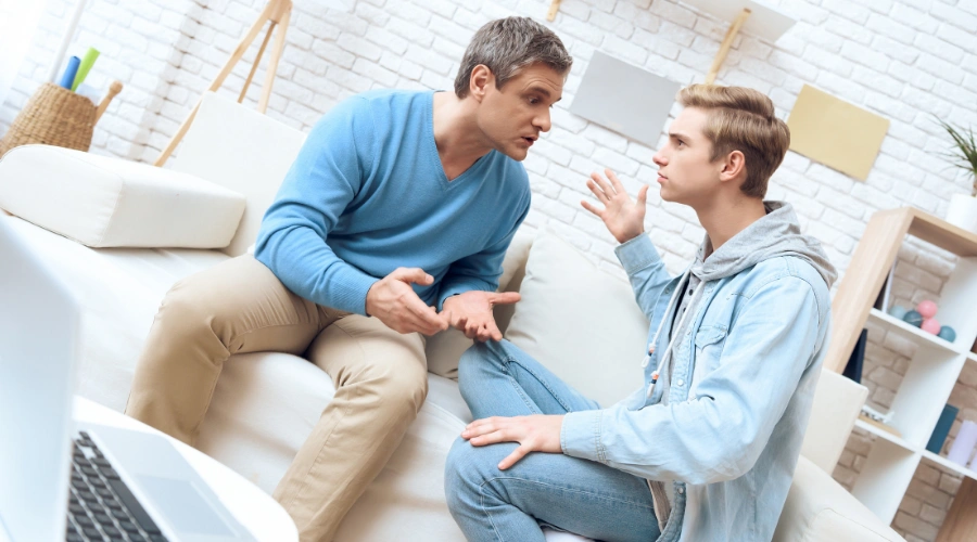 Image of a father and teenager sitting on a sofa in a heated discussion - Teen Anger Management - Artemis Adolescent Healing Center