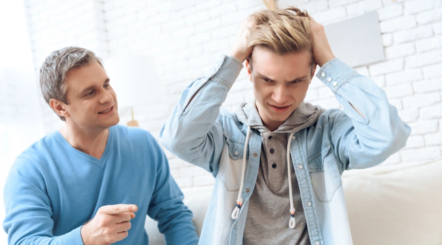 Image of a male teen looking anxious and withdrawn, illustrating the mental health impact of Xanax addiction, as his father looks on