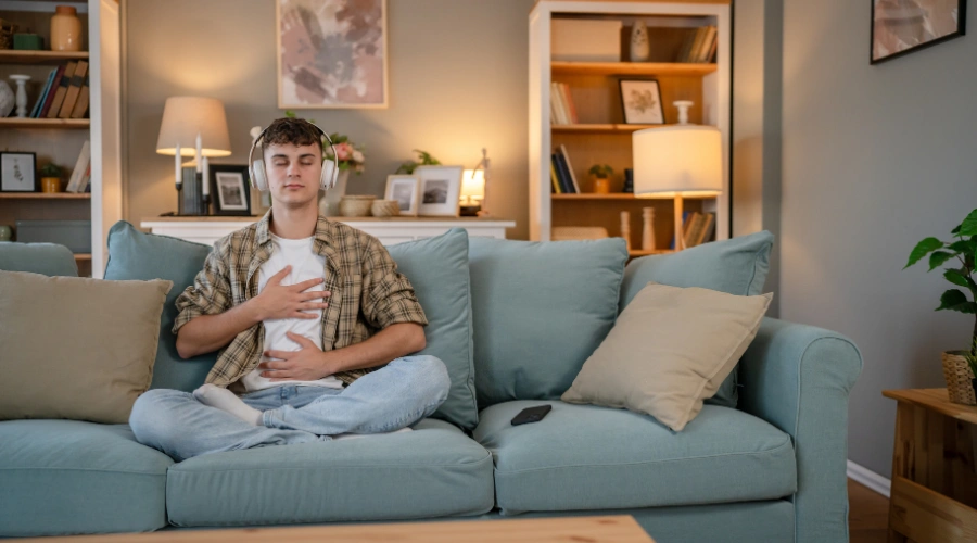 Image of a male teenager listening to music with headphones and sitting in a meditative position on a sofa