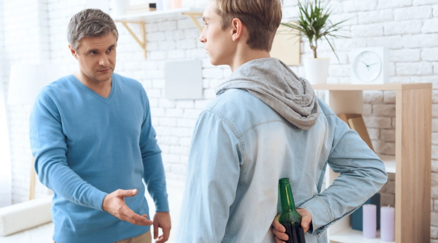 Image of a father questioning his teenage son, who is trying to hide a bottle of beer