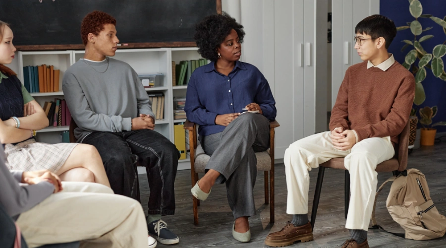 Image of teen attending an AA meeting, sitting among a supportive group during a recovery discussion