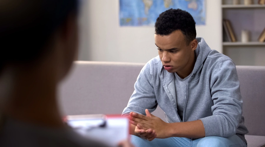 Image of a male teen sitting in therapy as his therapist looks on
