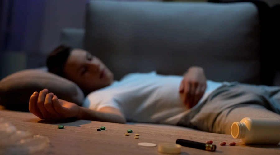 Image of a male teen passed out on abed besides opioid drugs and and stimulants
