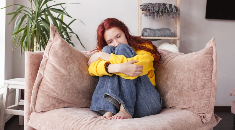 Image of a distraught female teen sitting in a chair with her face next to he knees - How to Identify The Signs of Psychosis in Teens - Artemis Adolescent Healing Center
