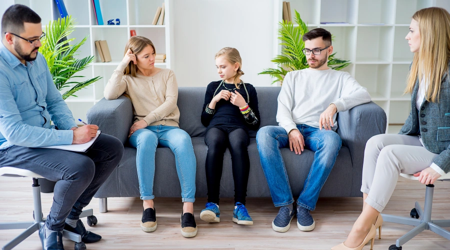 Image of a supportive mother and father sitting with their teen daughter and a pair of counselors in an addiction group therapy session