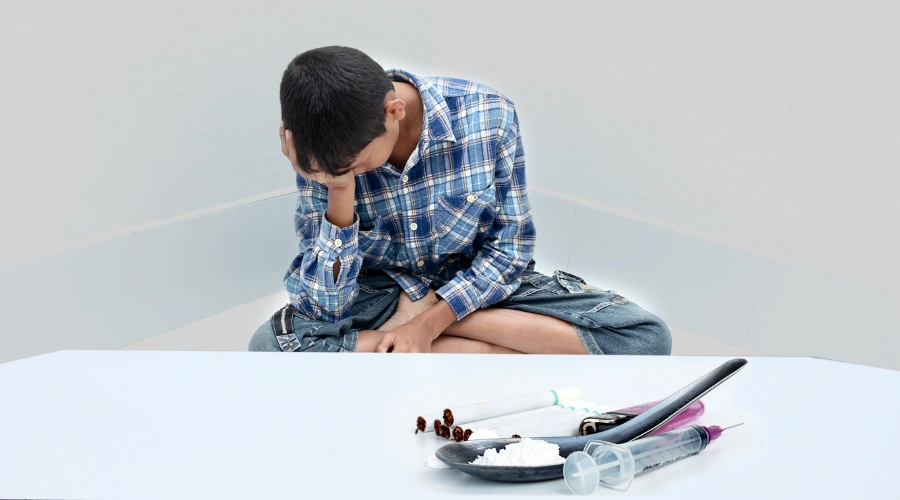 Image of a male teen sitting in despair in front of meth powder in a spoon and a syringe 