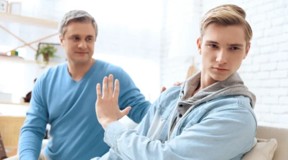 Image of a father trying to comfort an unhappy male teen, who is looking the other way with his hand up - Violent Behavior in Adolescence - Catalina Behavioral Health