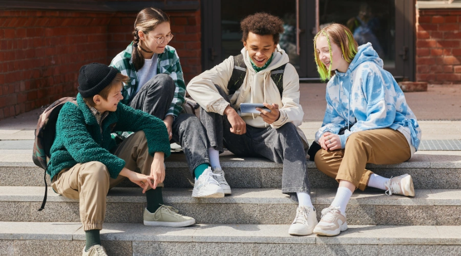 Image of 4 teens sitting on an outdoor stairway smiling and enjoying each other's company - Why Do Teens Skip School - Artemis Adolescent Healing Center