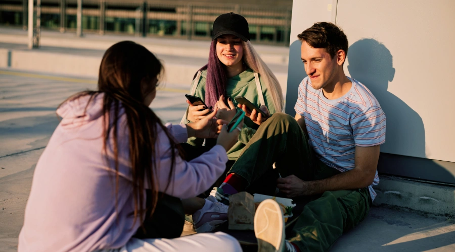 Image of teens sitting on the ground, interacting with their phones - A Parents’ Guide for Teen Slang on Drugs, Drinking, and Mental Health Issues - Artemis Adolescent Healing Center