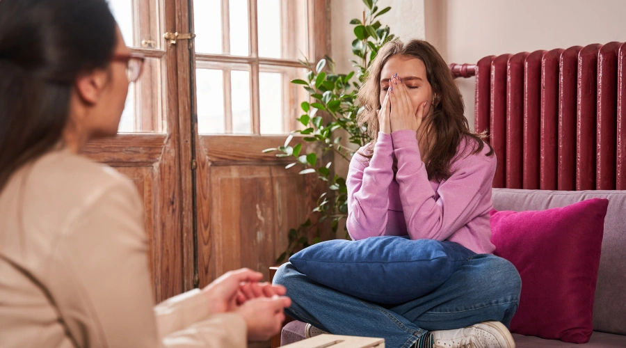 Image of female teen sitting on a sofa with her hands over her mouth, in a therapy session with a counselor - Teen Histrionic Personality Disorder Treatment - Artemis Adolescent Healing Center