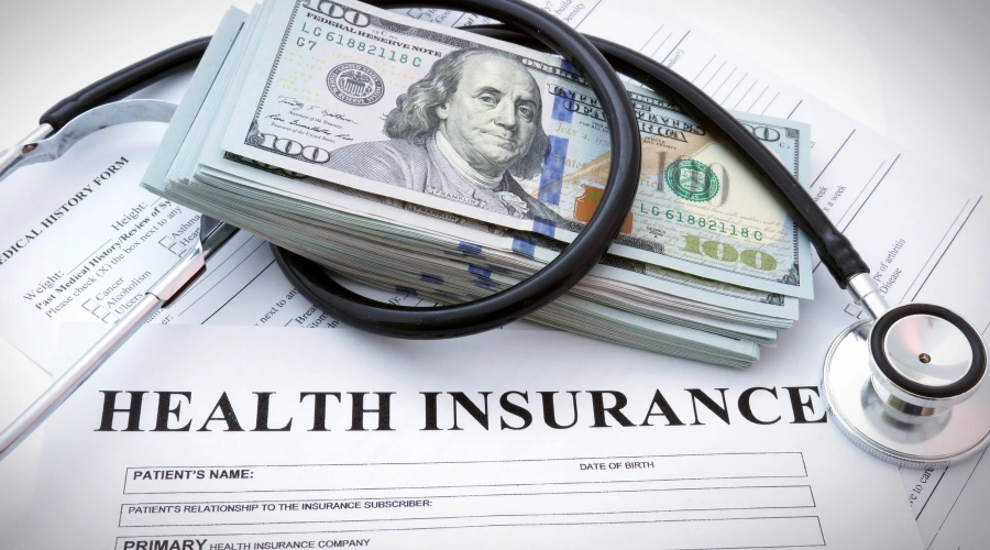 Image of a health insurance form with a stethoscope and stack of hundred-dollar bills