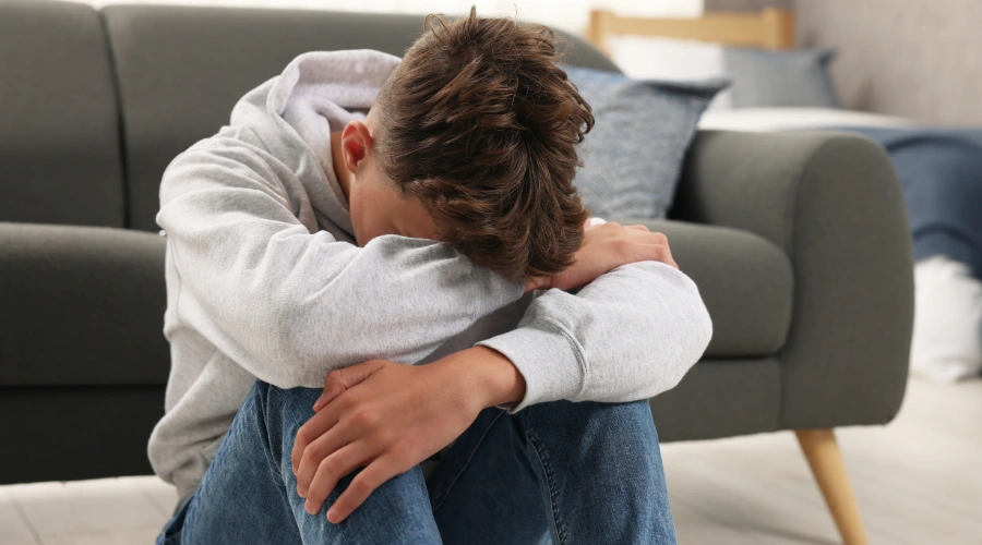 Image of a lonely teenage boy sitting on the floor with his head buried in his arms, shows the concept of Cigna teen rehab coverage