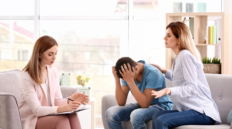 Image of a therapist taking notes while counseling a distressed teenage boy during a family therapy session shows the concept of aetna coverage for teen dual diagnosis treatment